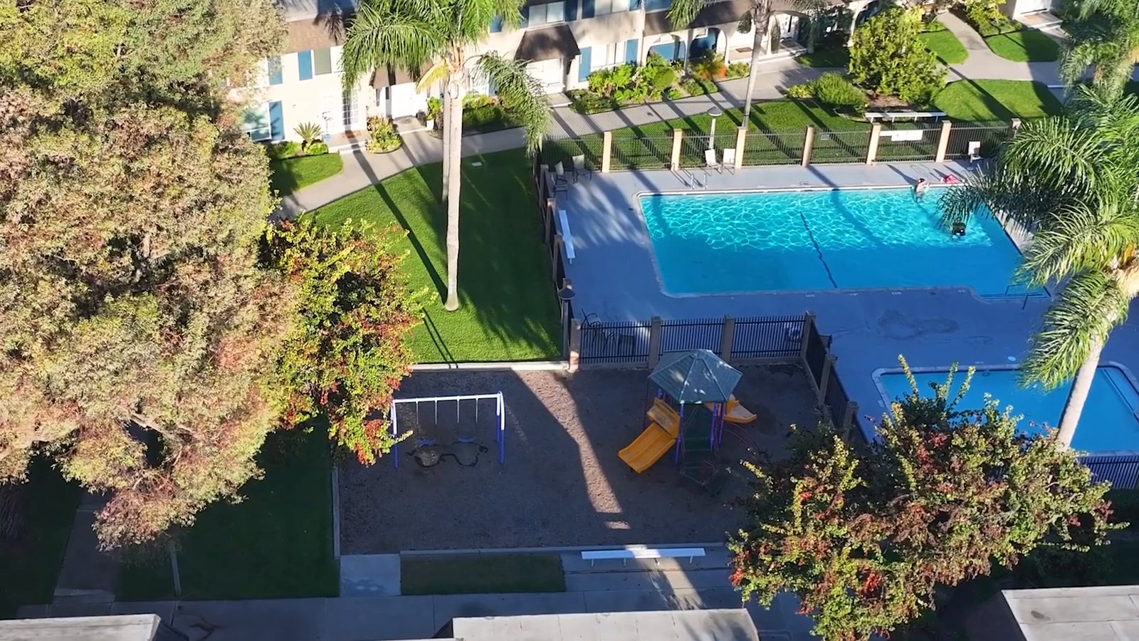 Aerial view over Cypress Tanglewood — the pool, the playground and the palm-lined greenbelt on a clear afternoon