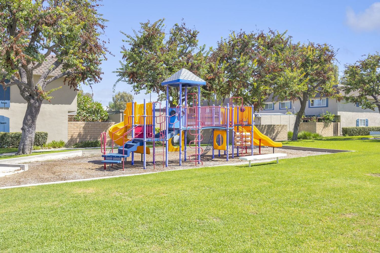 A brightly coloured playground set on the lawn between townhomes